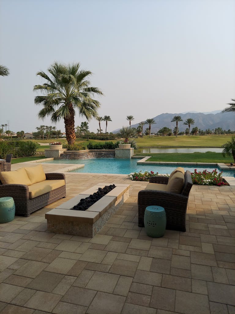 Sunny outdoor patio with poolside view, palm trees, and cozy seating at a tropical resort.